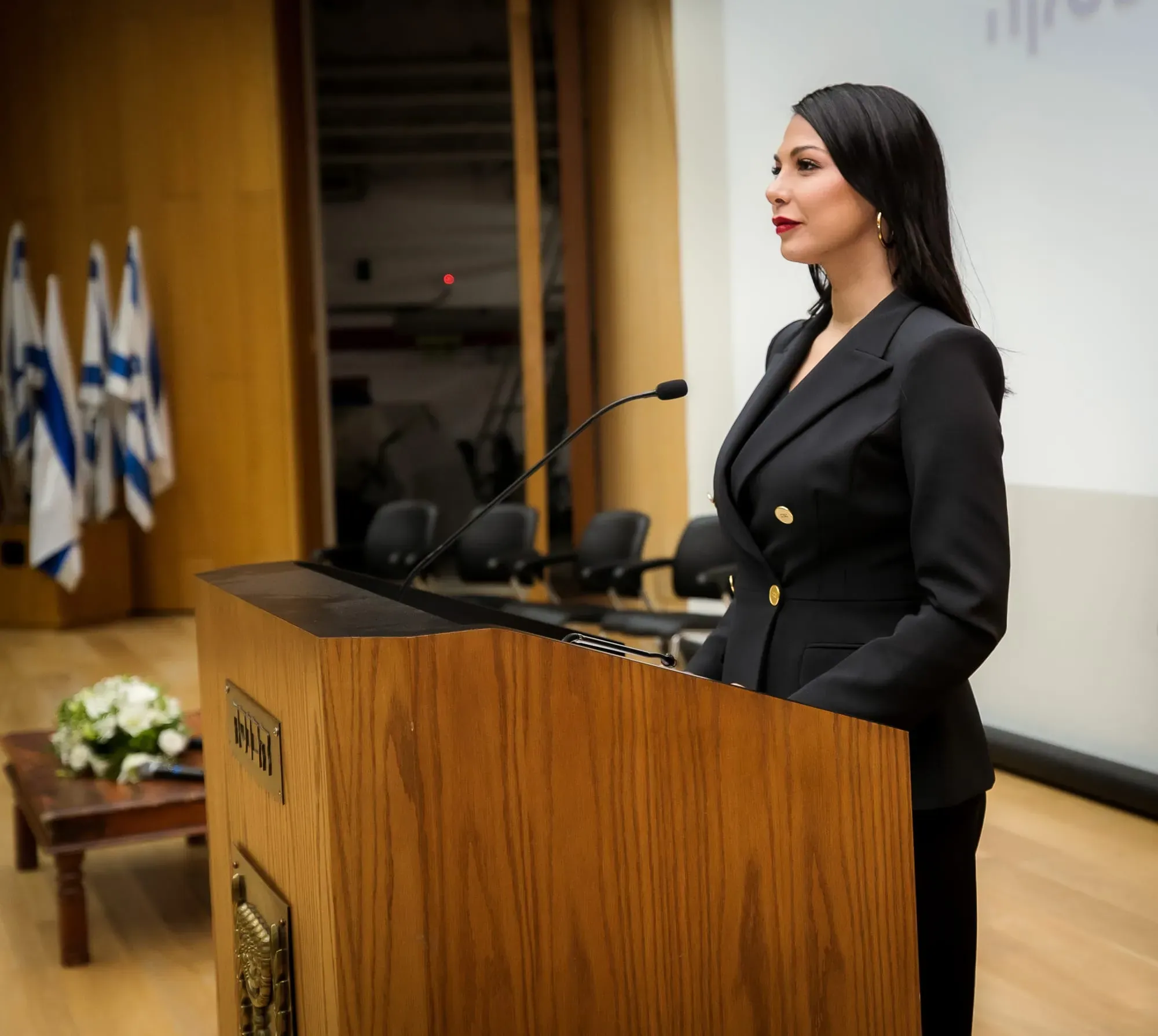 צילום אירוע: מורן אטיאס ליד דוכן באולם עם דגלי ישראל