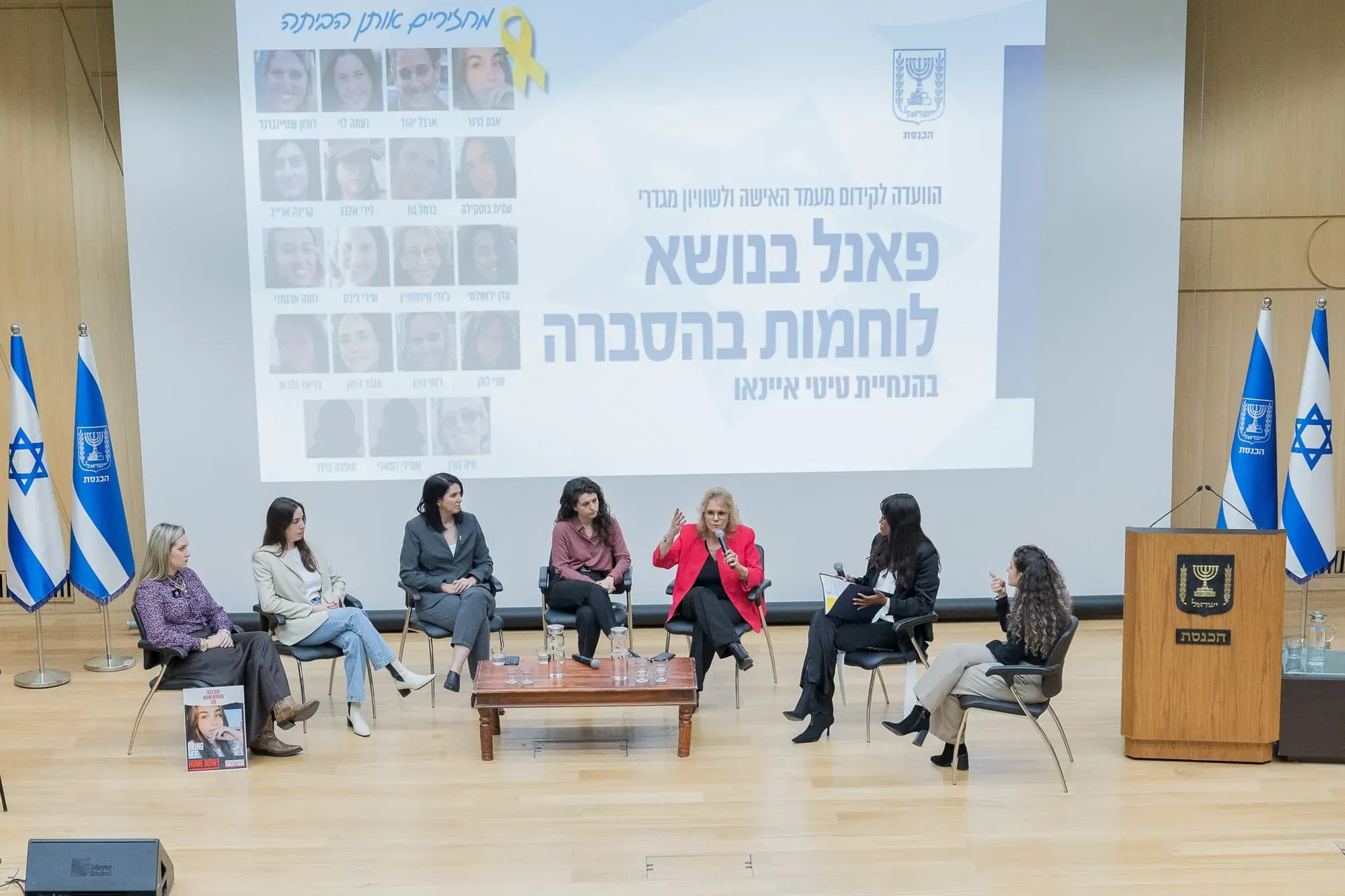 פאנל נשים באולם הרצאות, מסך עם כותרת על נושא החטופים