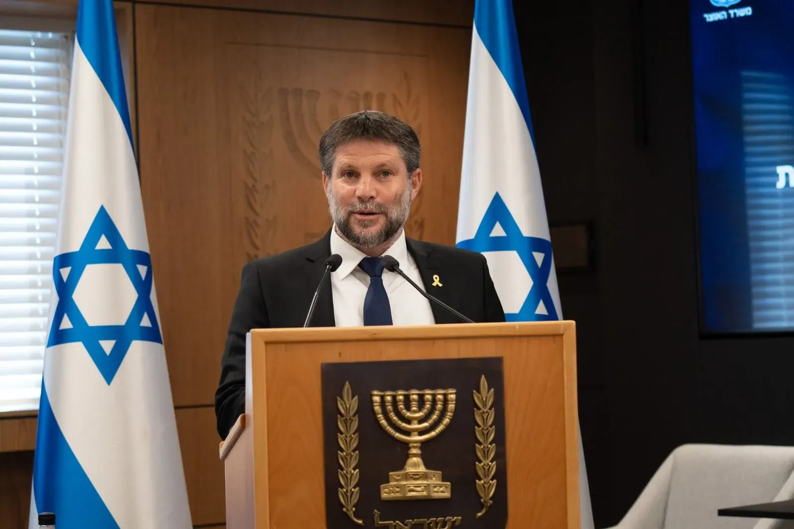 צילום אירוע: בצלאל סמוטריץ' נואם ליד דוכן עם דגלי ישראל