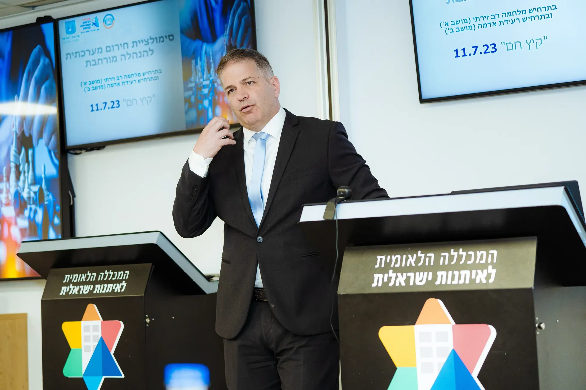 גבר בחליפה מדבר בכנס ממול דוכנים של רשות הכנסת הלאומית