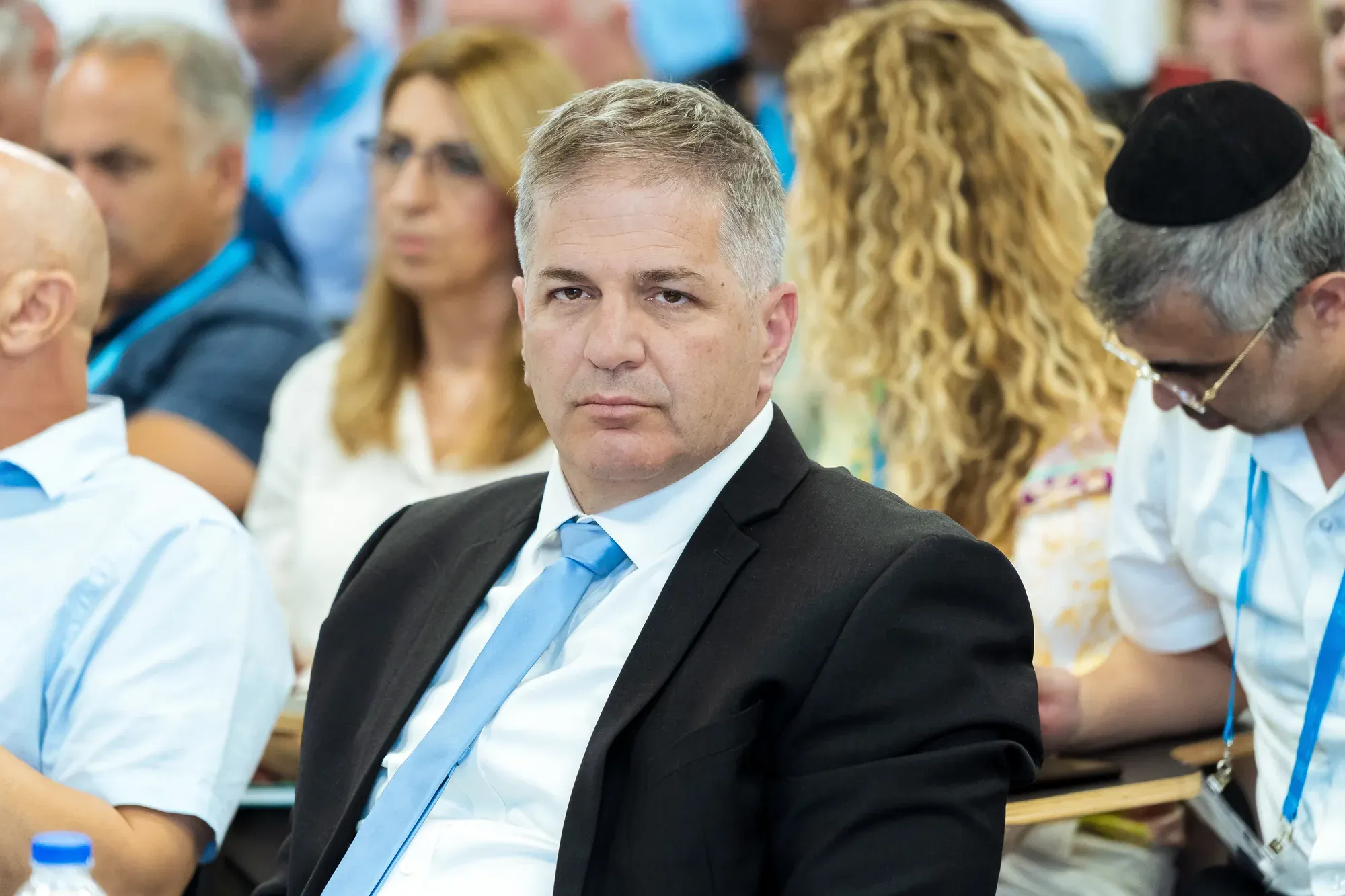 גבר בחליפה וחולצה כחולה יושב בקהל בכנס