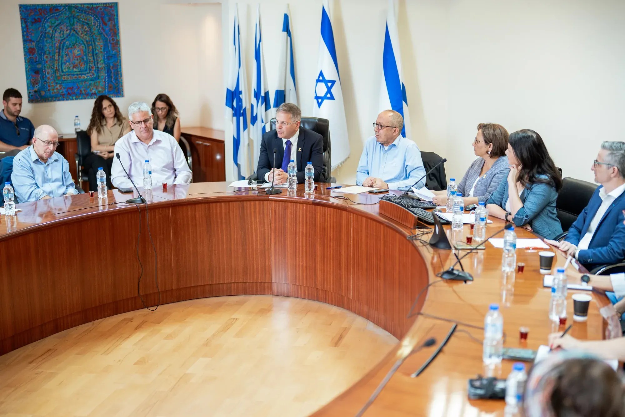 ישיבת ועדה בחדר ישיבות מעוגל עם דגלי ישראל
