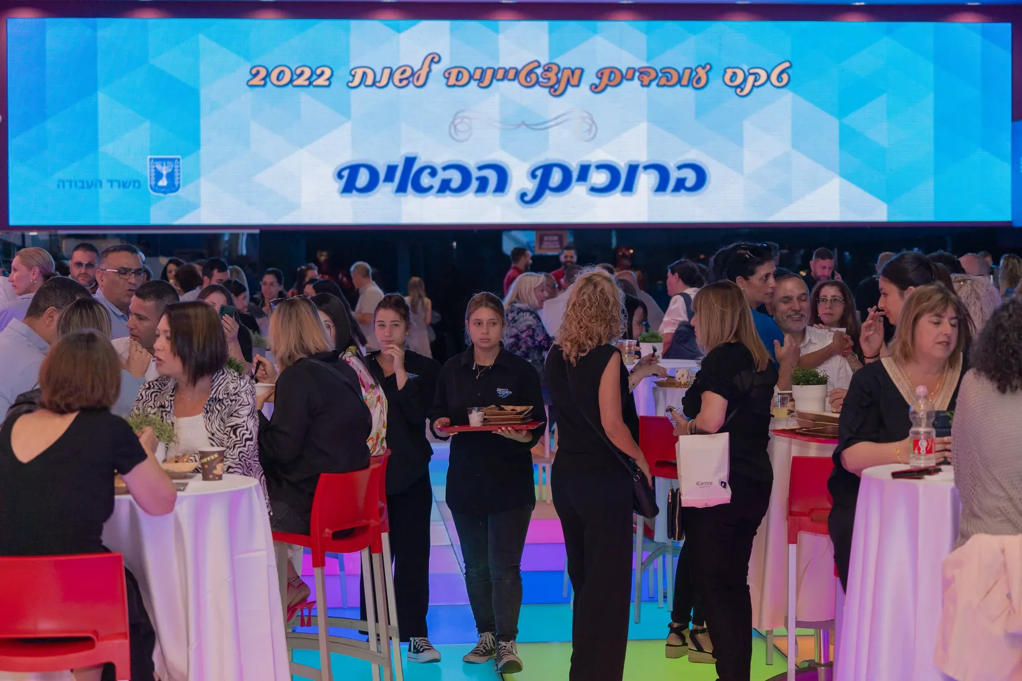 קהל באולם אירוע חגיגי עם שלט ברוכים הבאים