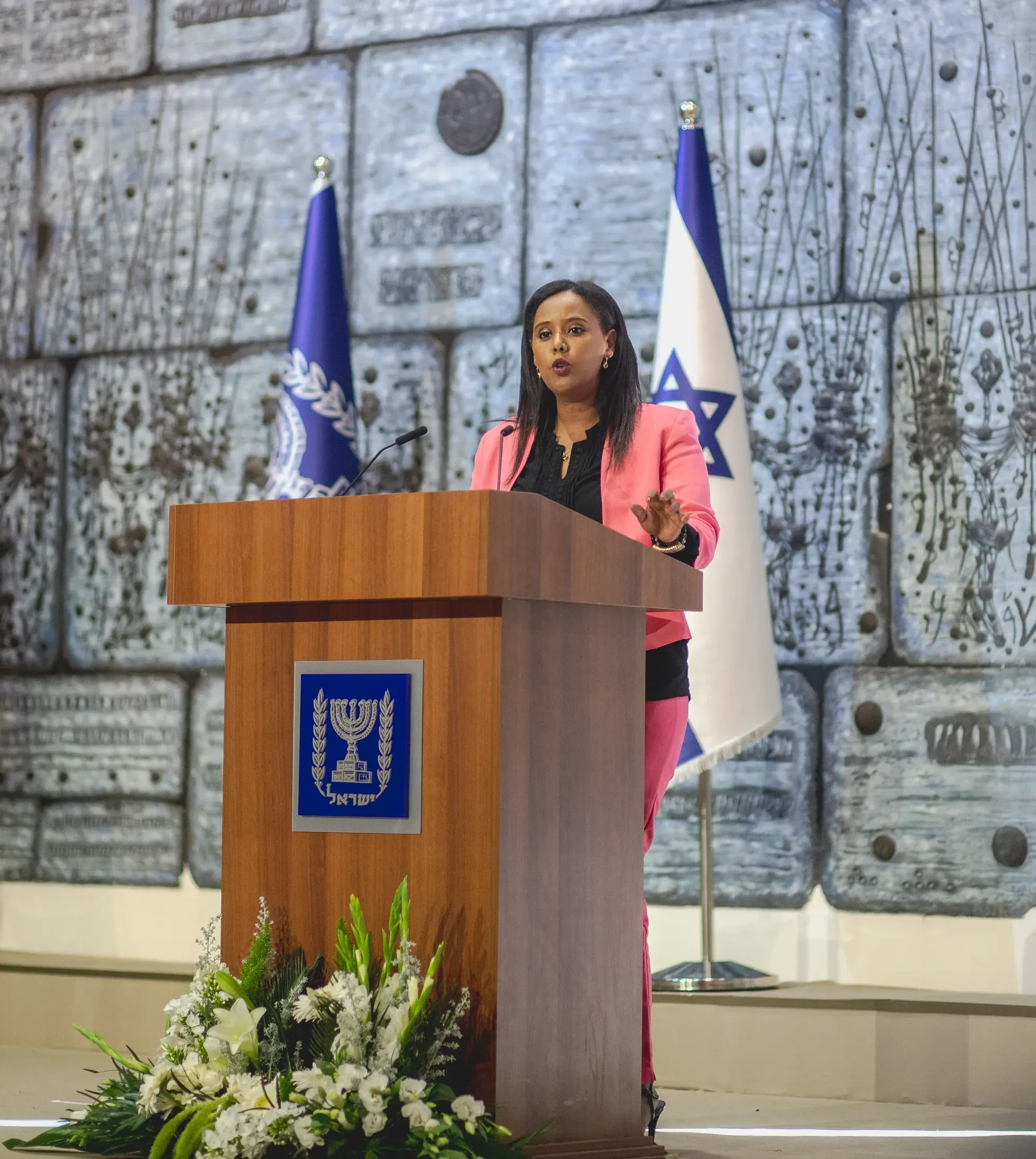 צילום אירוע: פנינה תמנו שטה נואמת ליד דוכן עם סמל המדינה