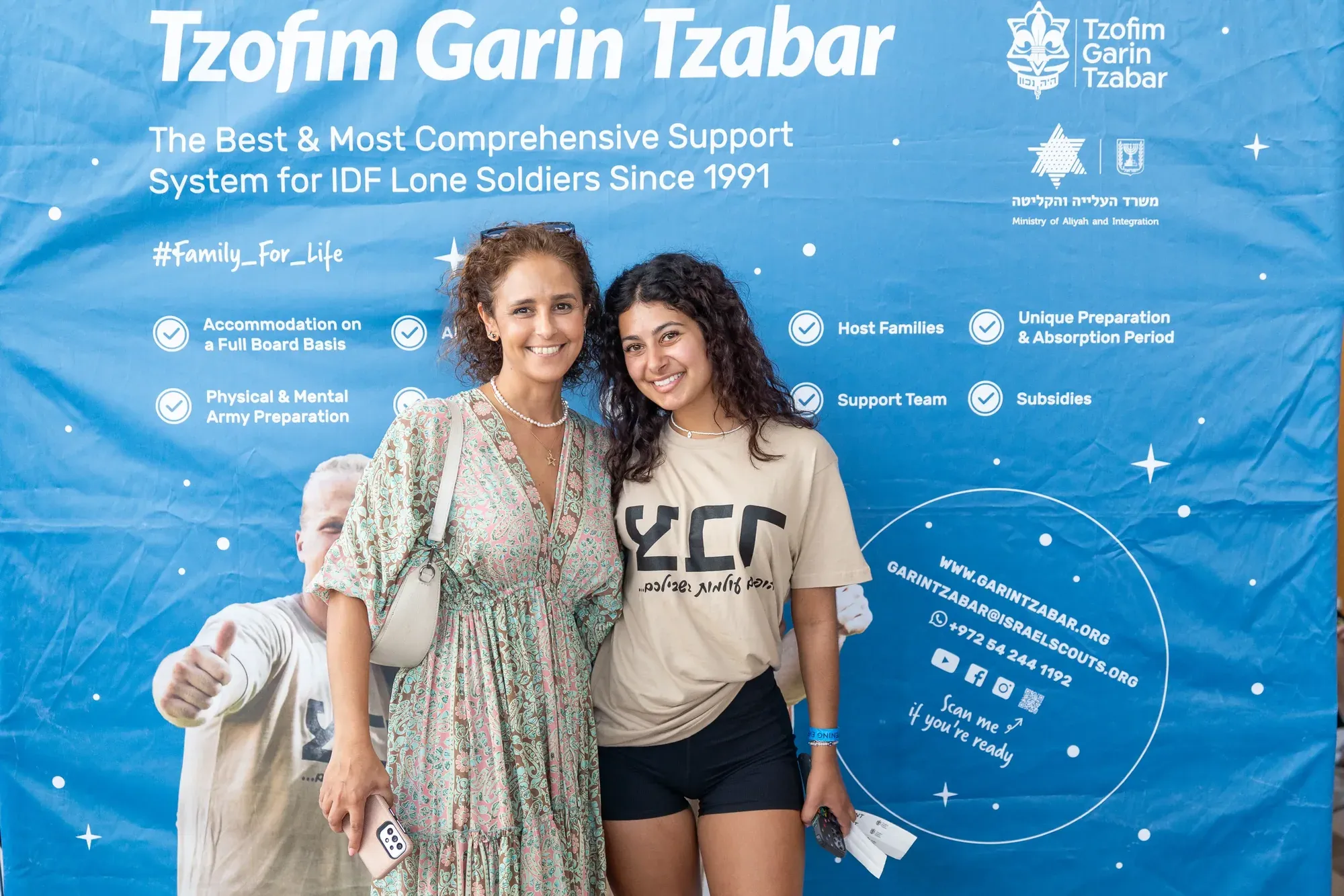 אם ובתה מצטלמות עם מתנדבת ליד שלט האירוע