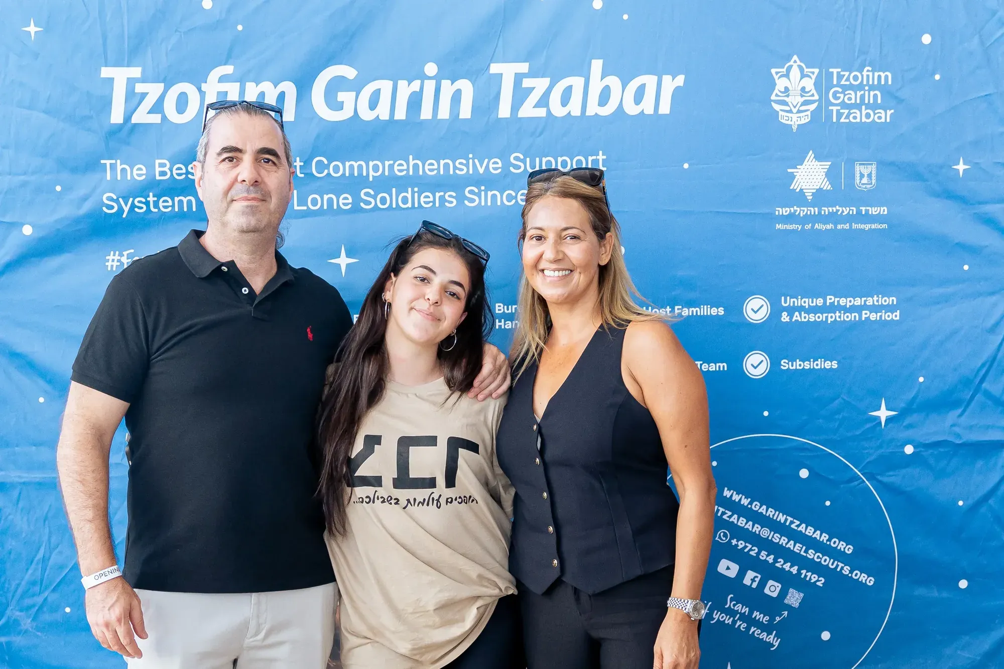 משפחה ומתנדבת מצטלמות ליד שלט של עמותת חיילים בודדים
