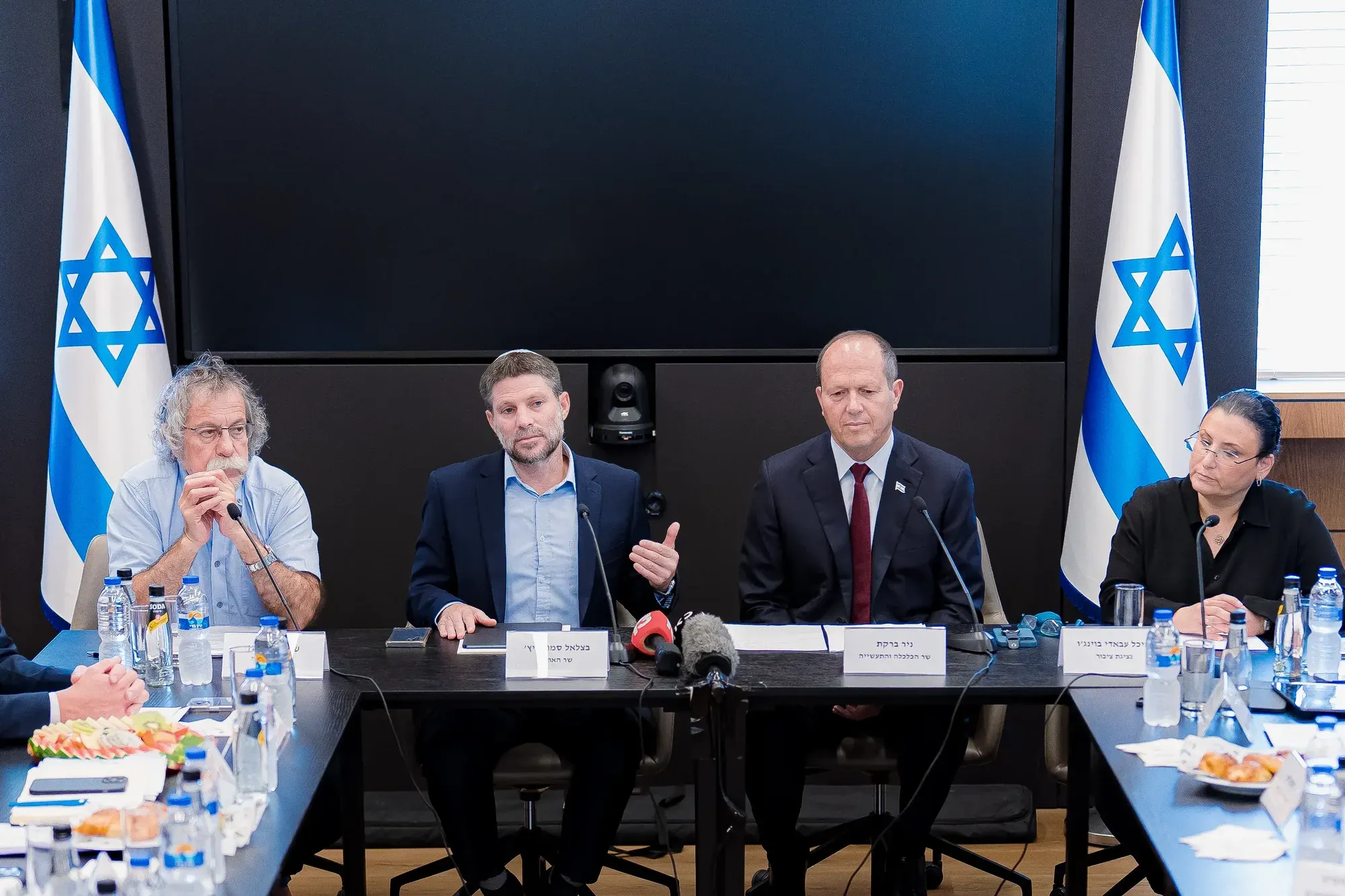 מסיבת עיתונאים של בכירים מאחורי שולחן עם דגלי ישראל