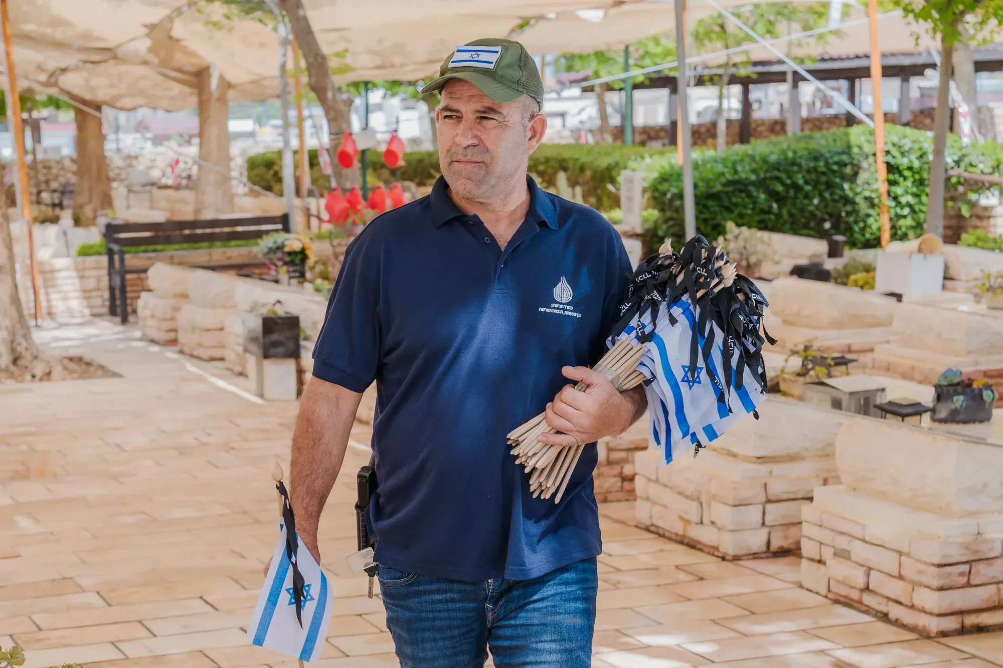 אדם עם כובע מחזיק דגלי ישראל קטנים בבית קברות צבאי