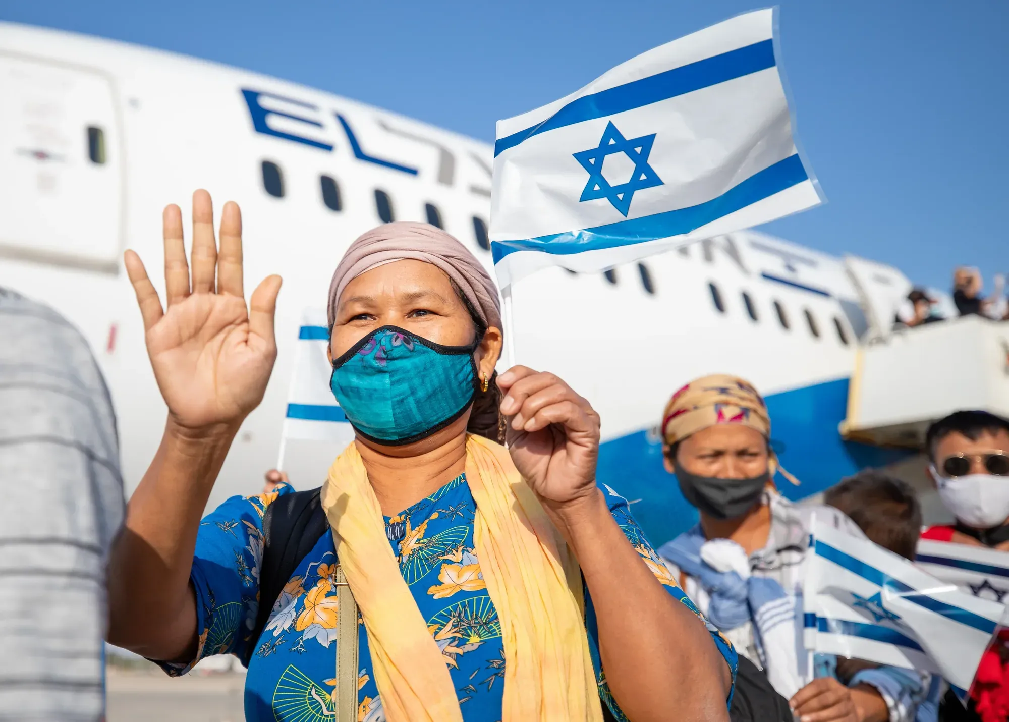 אשה עולה עם צעיף צבעוני ומנופפת בשמחה על רקע מטוס אל על