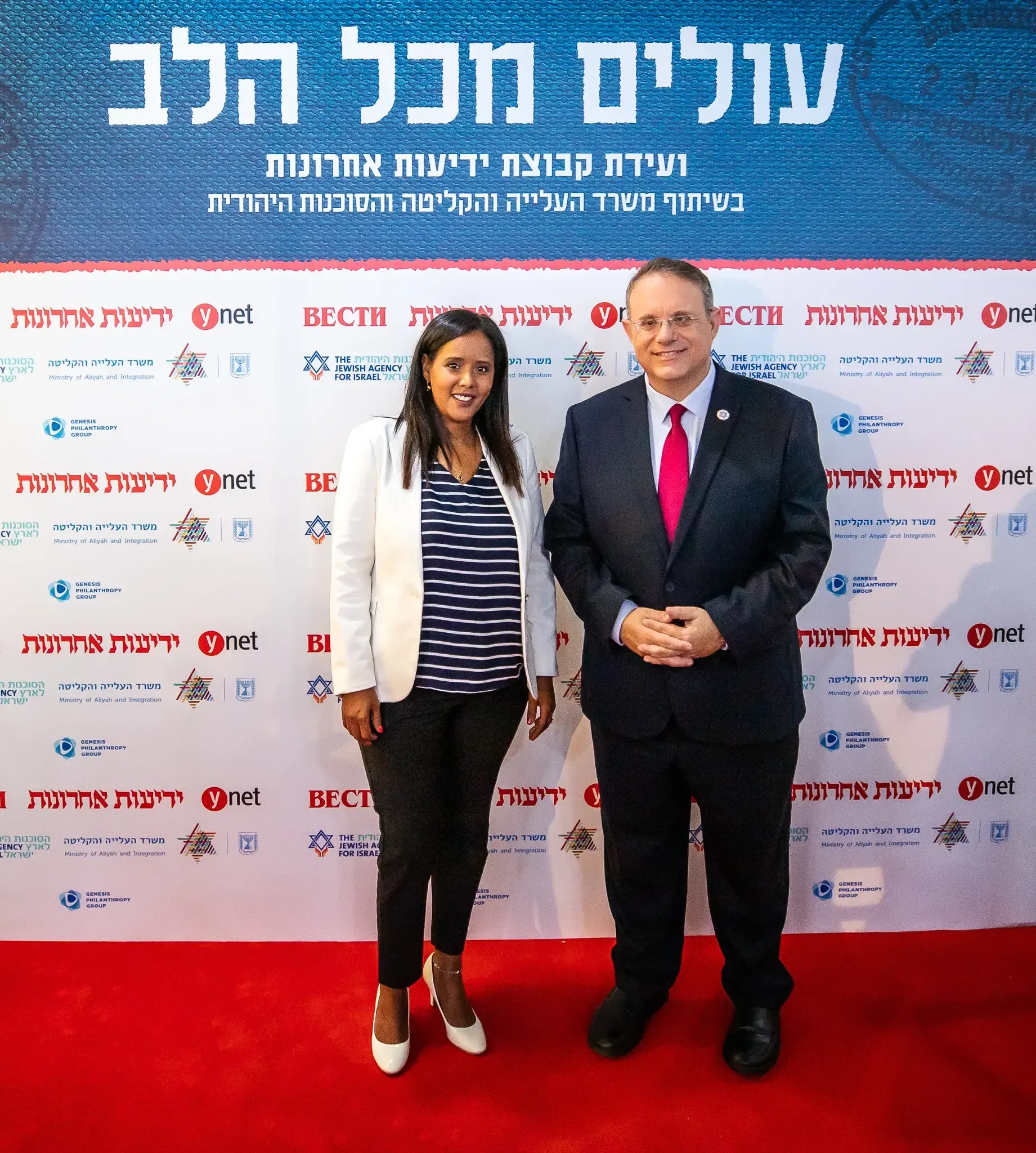 שתי דמויות מצטלמות על שטיח אדום מול קיר חסויות עולים