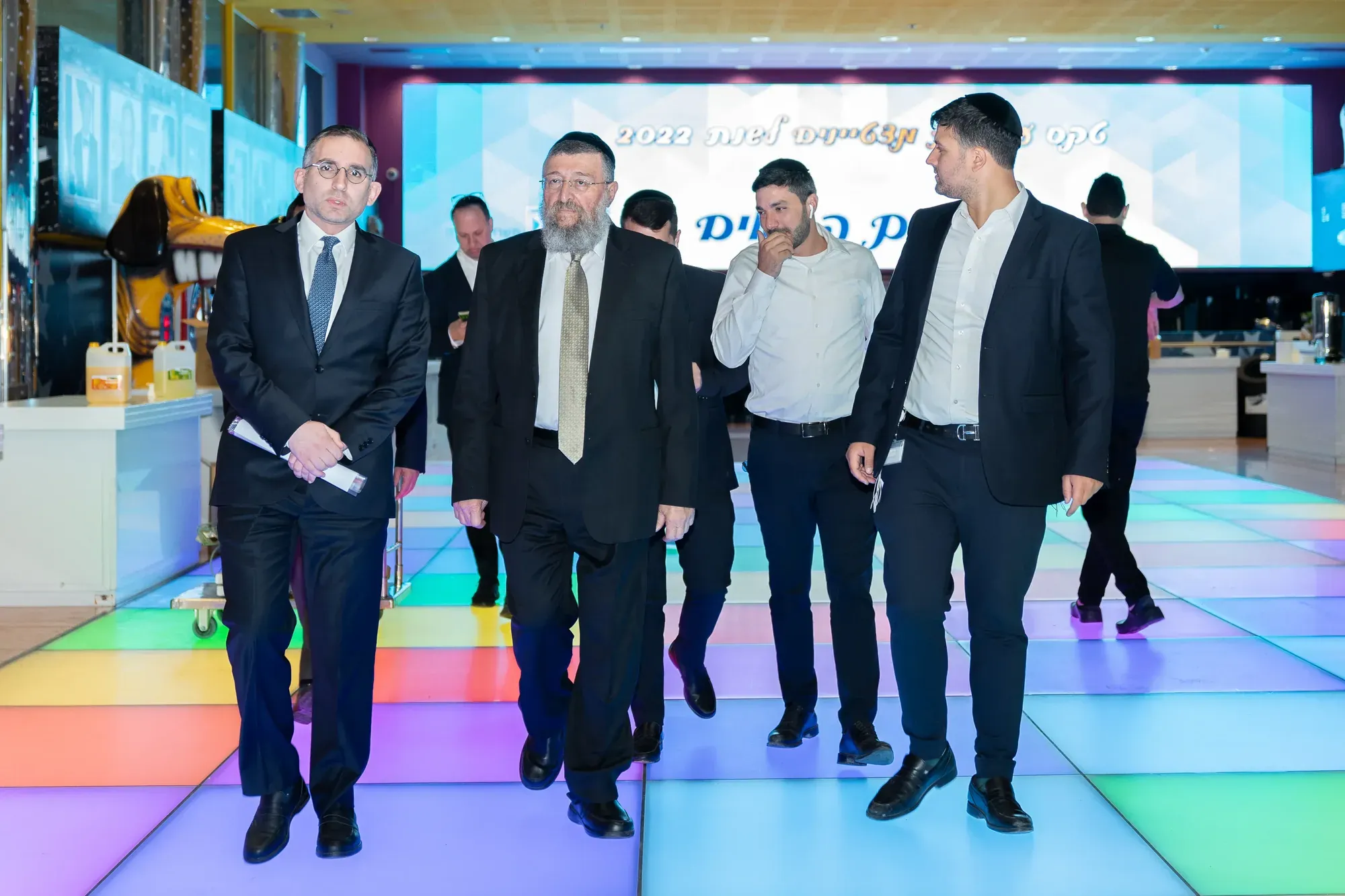 אנשים בחליפות צועדים על רצפה מוארת בצבעים באירוע
