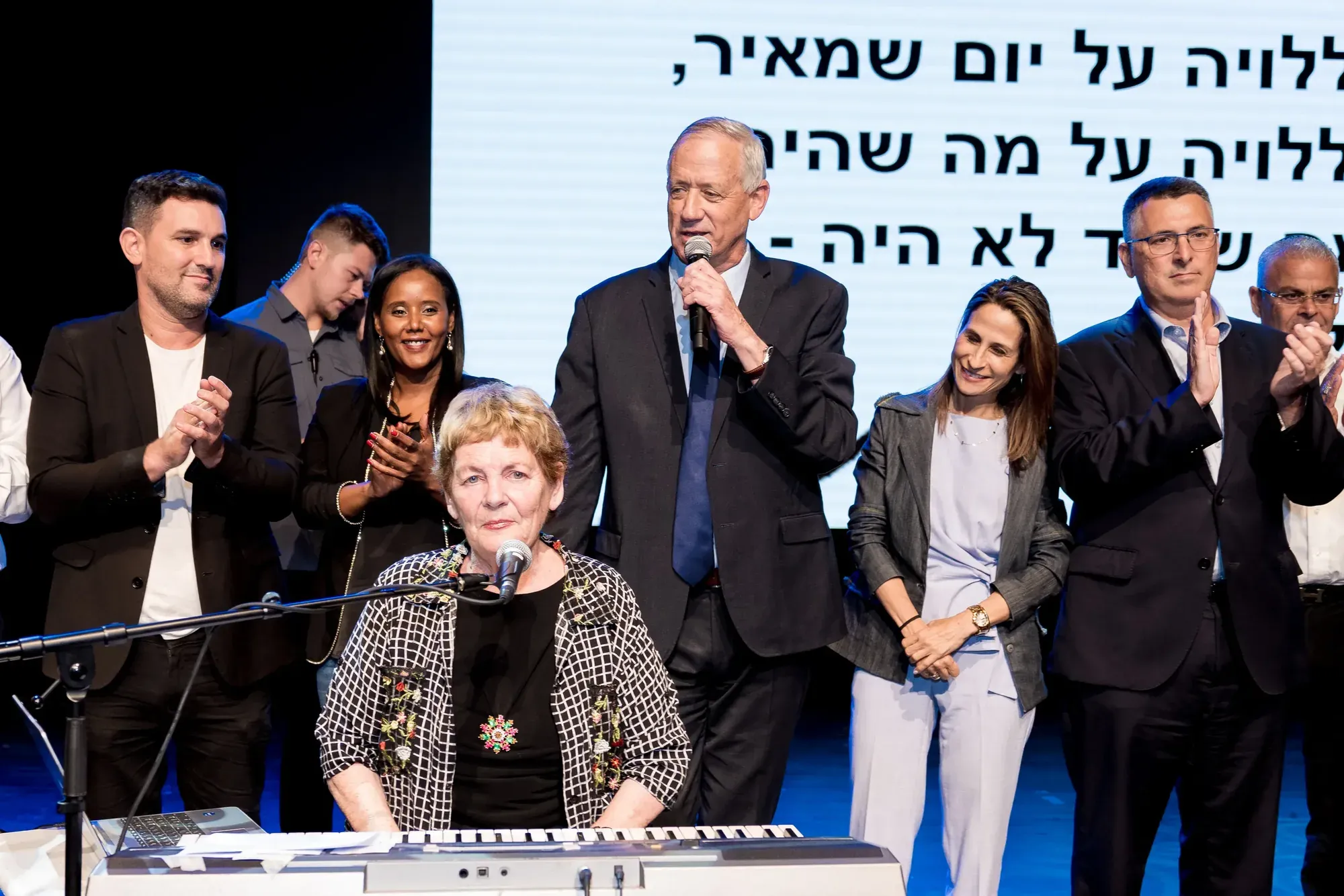 מוזיקאית וזמרים מובילים שירה משותפת על במה, מילות שיר על מסך