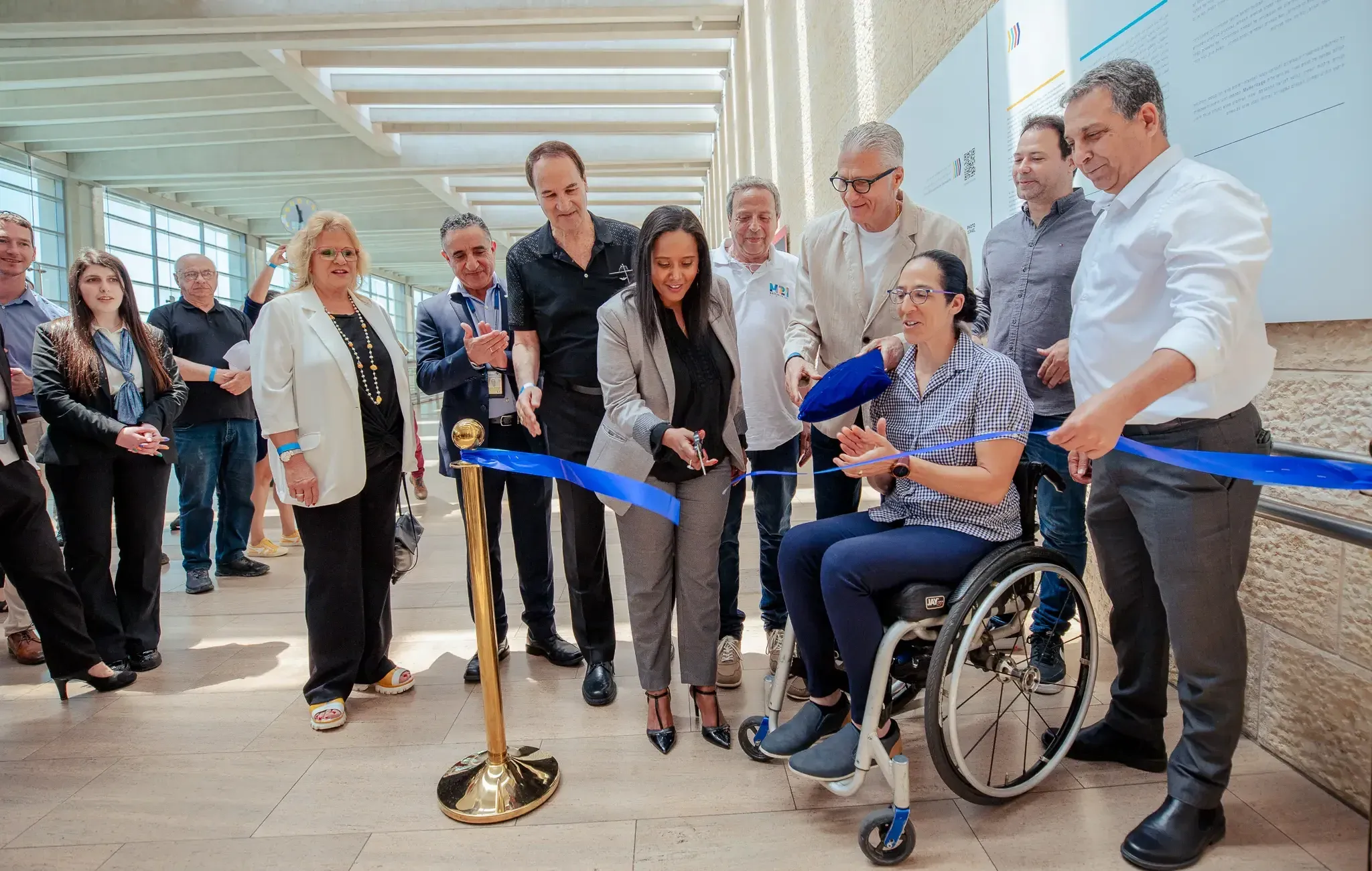 גזירת סרט חגיגית במסדרון עם קבוצת אנשים ואדם בכיסא גלגלים