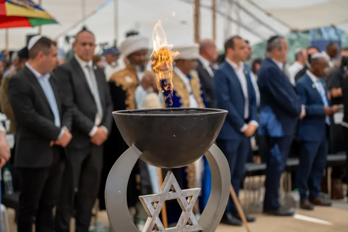 אנשים עומדים בטקס זיכרון ליד כלי הדלקת אש בצורת מגן דוד