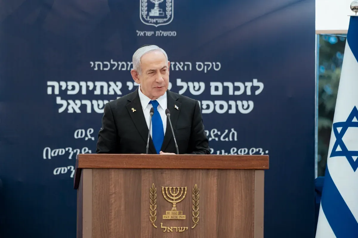 נואם בחליפה ליד דוכן עם סמל המדינה, ברקע שלט בעברית ובאמהרית