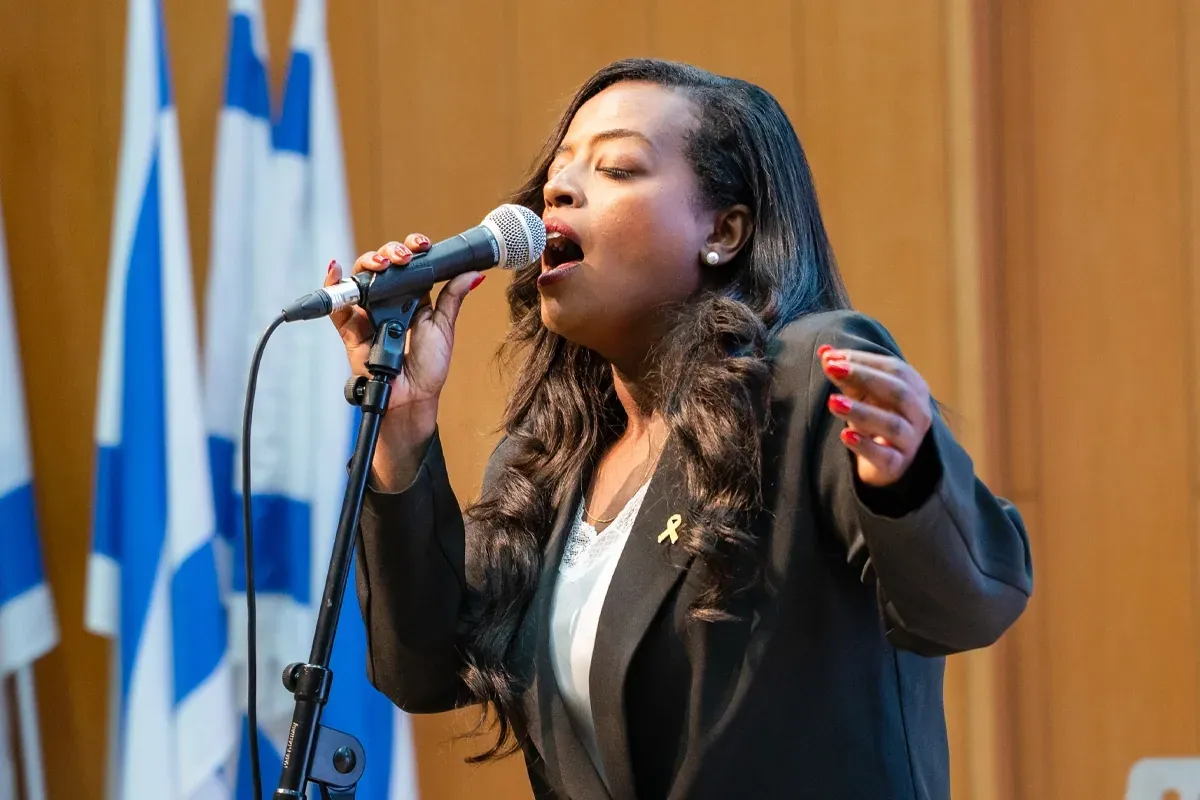 זמרת שרה בהתלהבות עם מיקרופון, דגלי ישראל מאחוריה