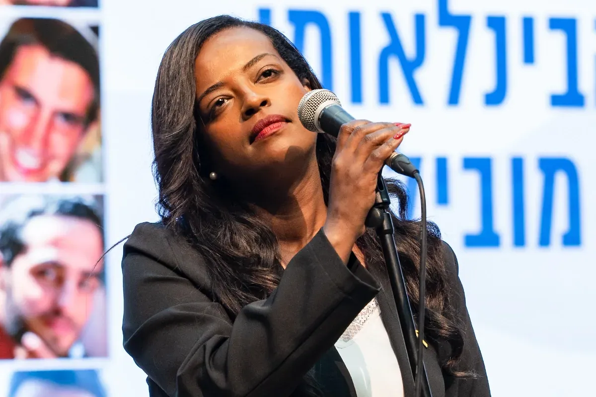 זמרת שחורת שיער שרה לתוך מיקרופון באירוע בהשתתפות תמונות חטופים