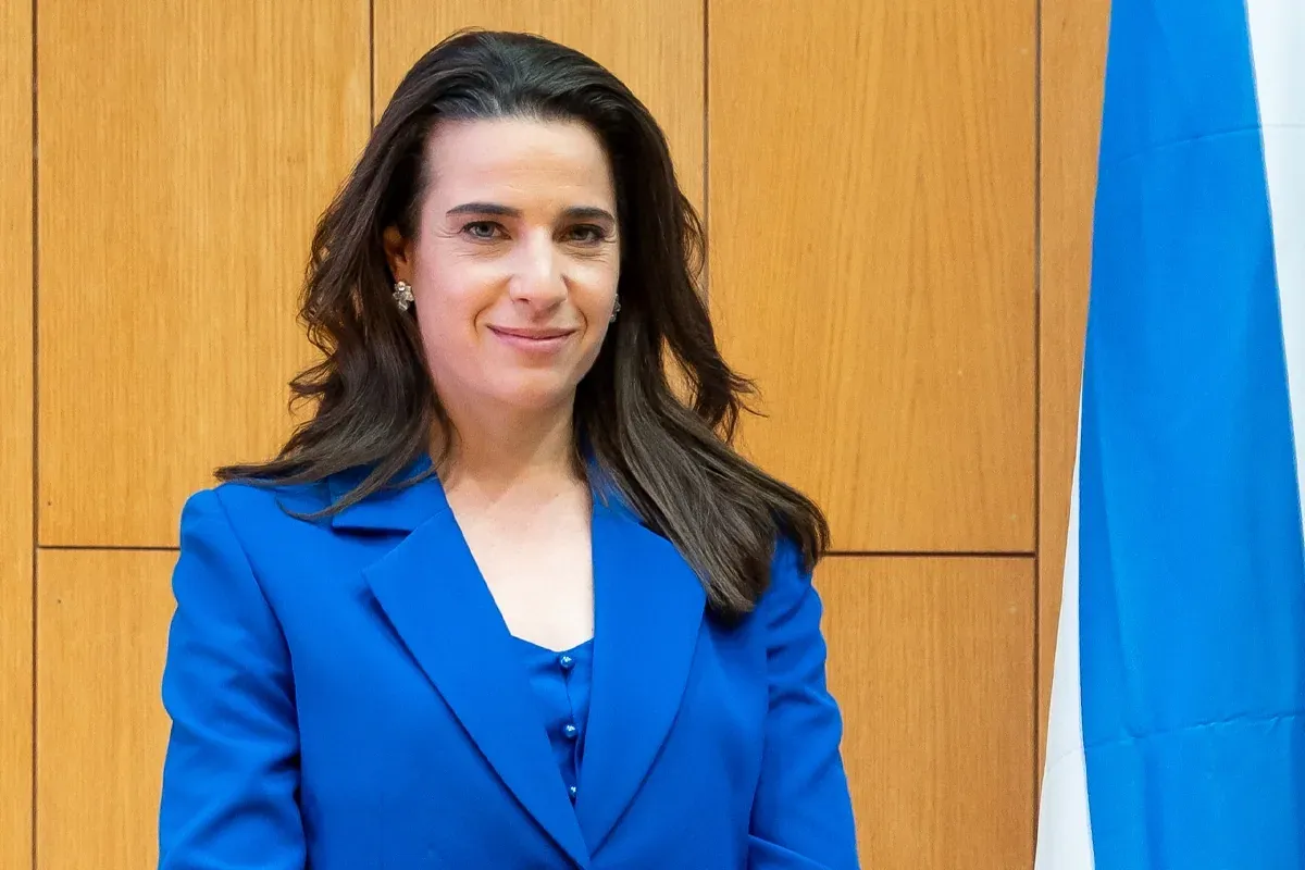 פורטרט של אשה בחליפה כחולה על רקע עץ ודגל