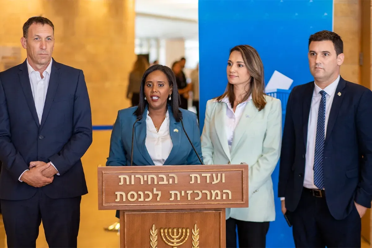 שלושה אנשים בחליפות מצטלמים ליד דוכן ועדת הבחירות המרכזית