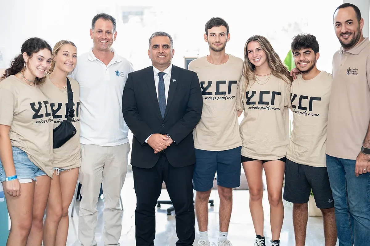 קבוצת מתנדבים עם חולצות זהות מצטלמת עם אורח רשמי