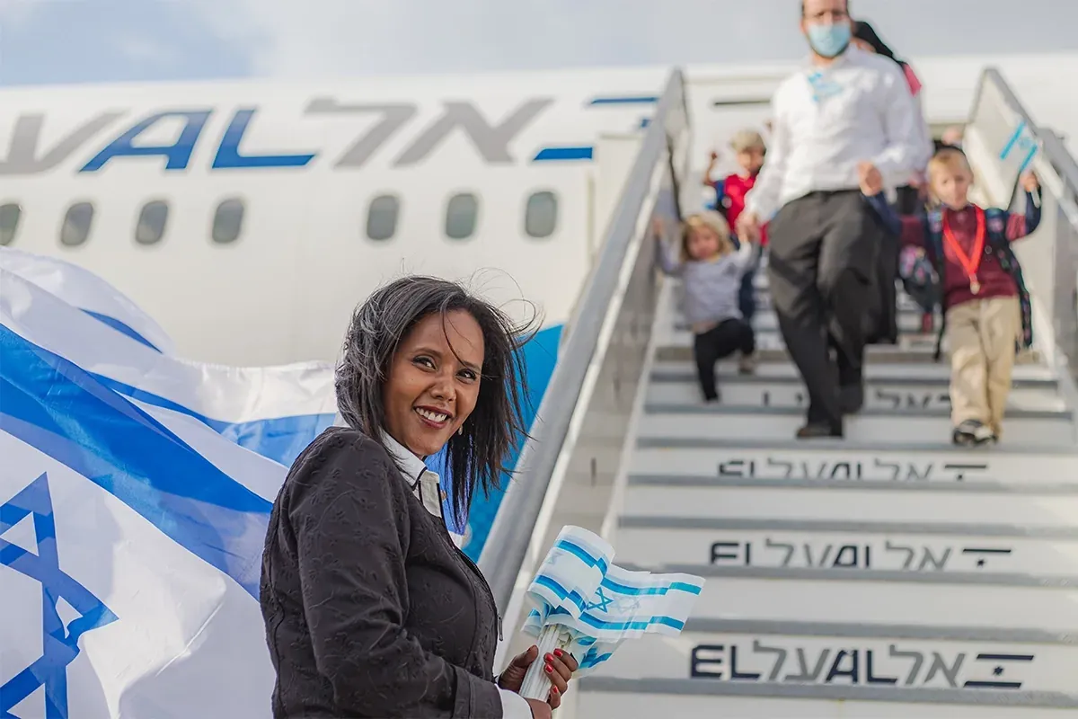 אשה מחייכת עם דגל ישראל על מדרגות מטוס אל על, עולים יורדים מאחוריה