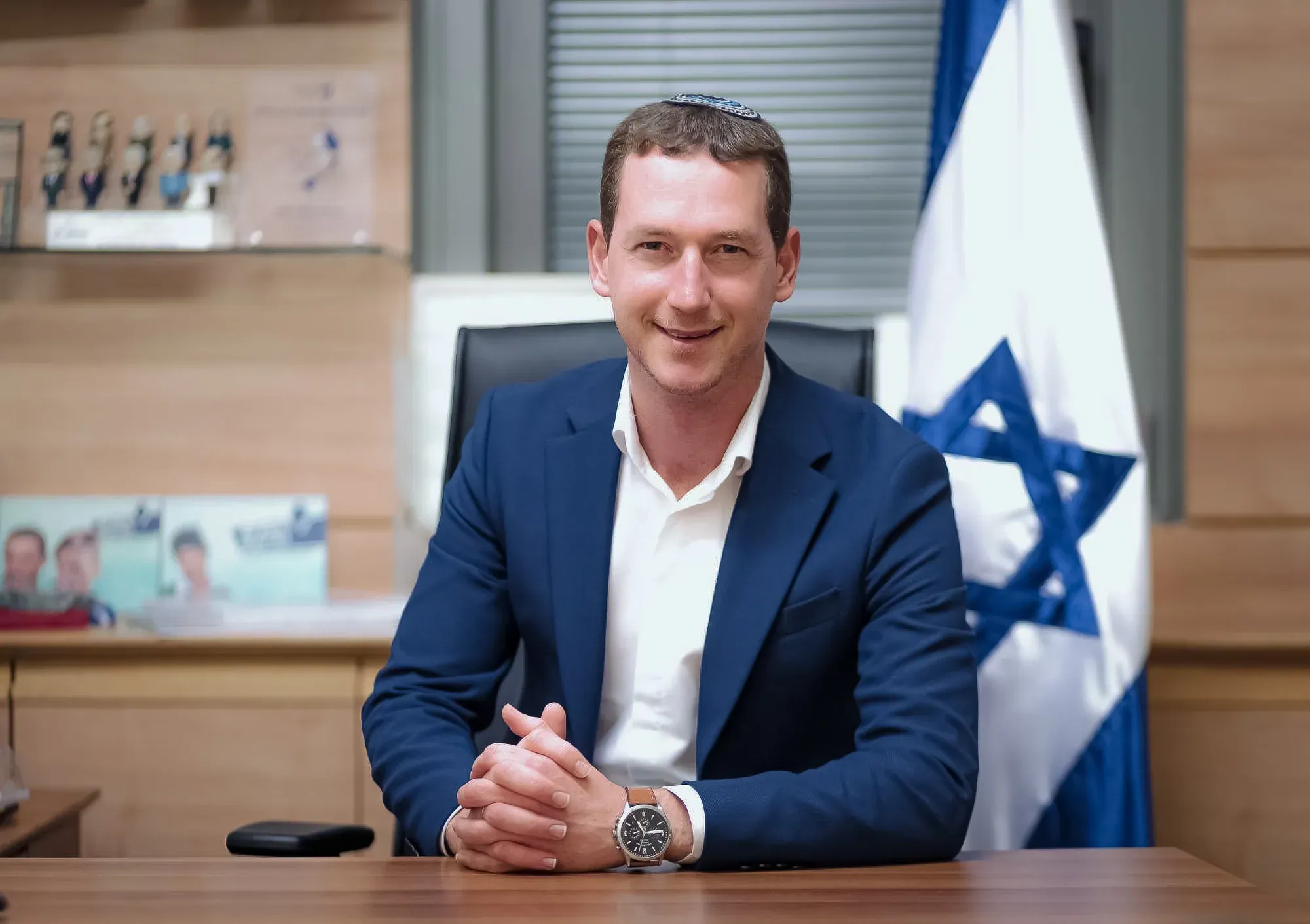 פורטרט עסקי של גבר בחליפה כחולה ליד שולחן ודגל ישראל