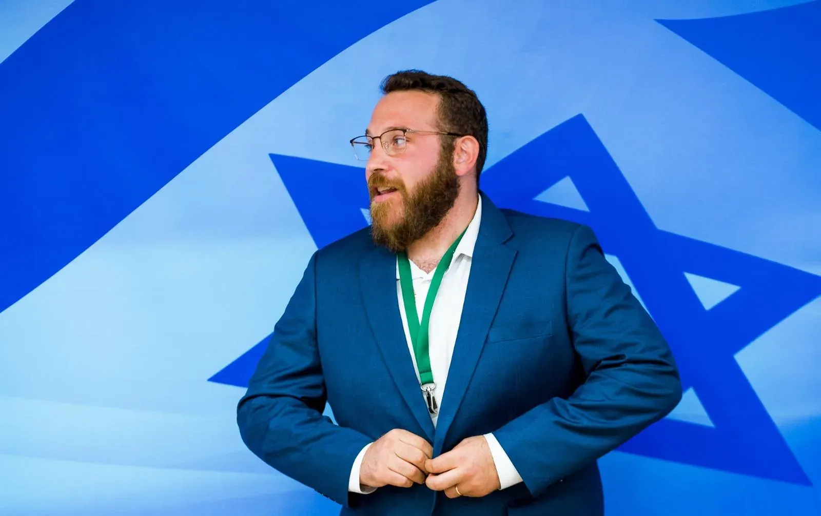 גבר עם זקן ותג כנס מסדר את הז'קט על רקע דגל ישראל גדול