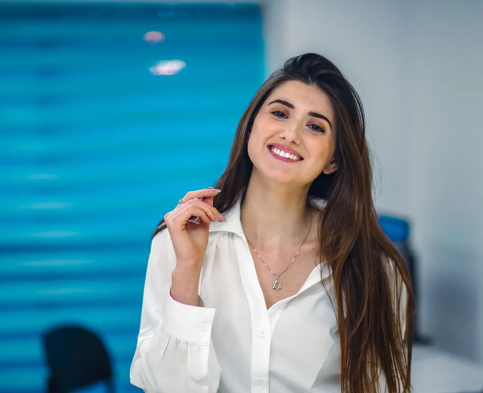 פורטרט של אשה צעירה מחייכת בחולצה לבנה על רקע כחול