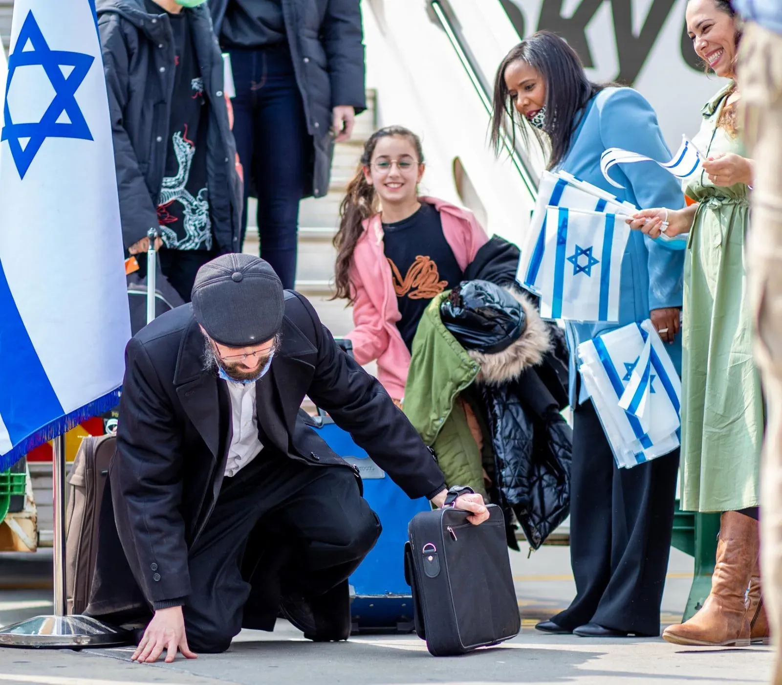 אדם כורע ברך ומנשק את האדמה בנחיתה בישראל, אנשים עם דגלים סביבו