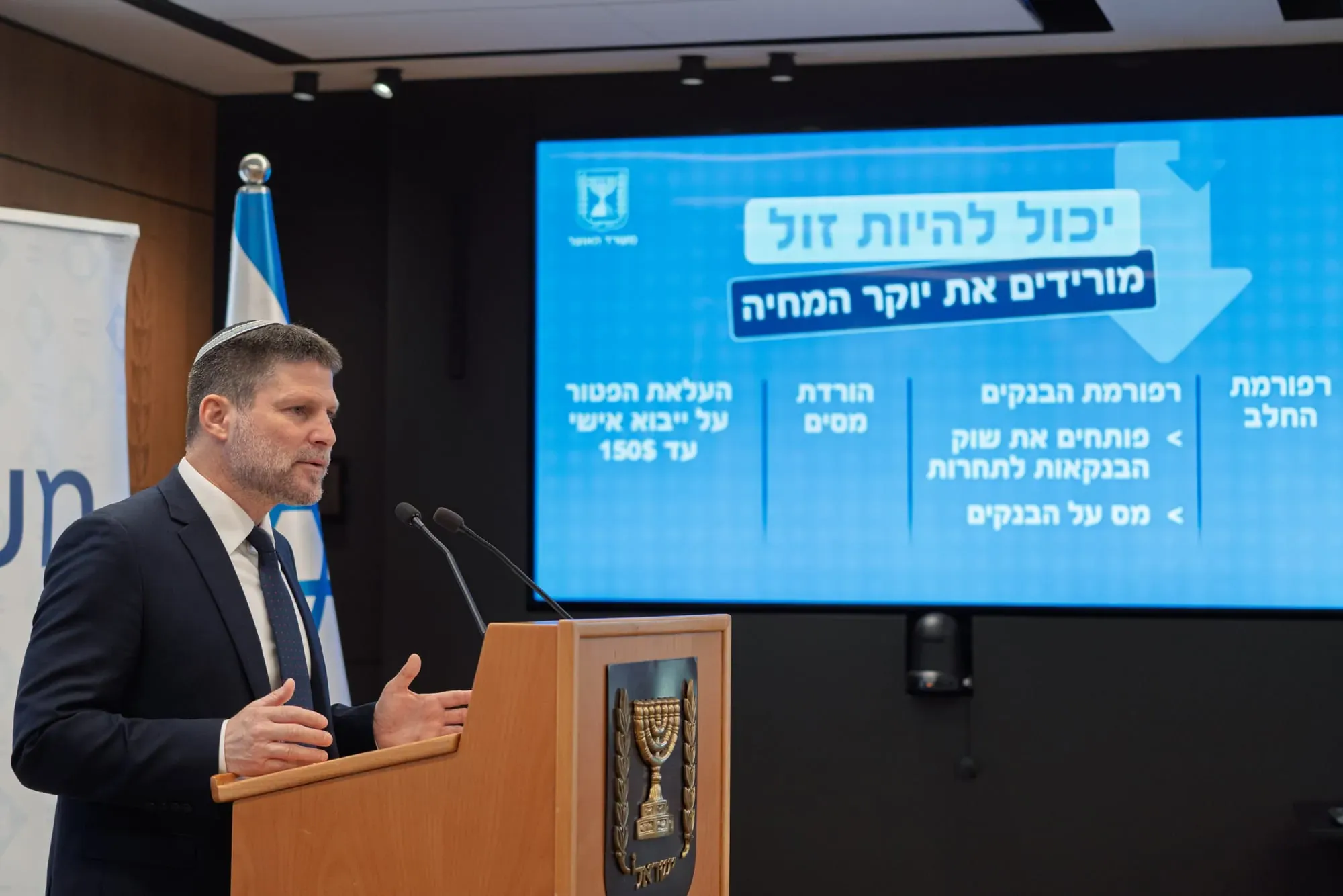 צילום אירוע: בצלאל סמוטריץ' נואם ליד הדוכן מול מסך מצגת עם דגל ישראל